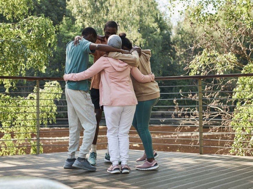 A small group of people embracing outdoors, supporting one another